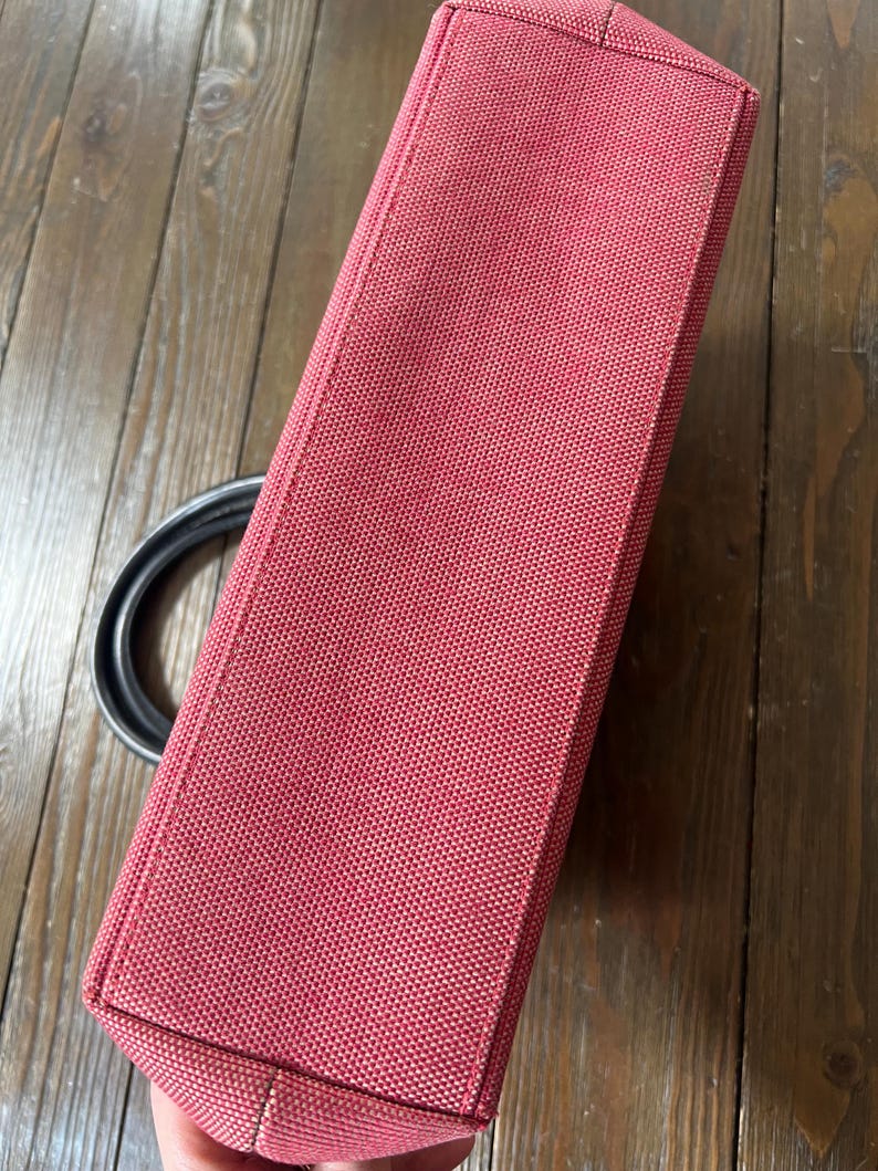 May include: A rectangular, red handbag with a textured fabric. The bag has a black handle and a structured design. The bag is made of a durable material and is suitable for everyday use.