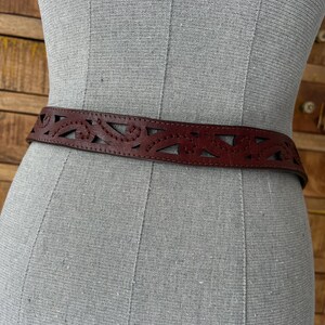 Peut inclure: Une ceinture en cuir marron avec un motif d&eacute;coup&eacute; d&eacute;coratif. La ceinture est pr&eacute;sent&eacute;e sur un mannequin, mettant en valeur son motif floral ou g&eacute;om&eacute;trique complexe. La ceinture est de couleur marron moyen.
