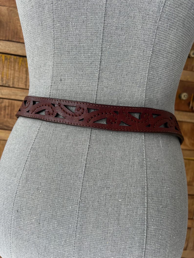 Peut inclure: Une ceinture en cuir marron avec un motif d&eacute;coup&eacute; d&eacute;coratif. La ceinture est pr&eacute;sent&eacute;e sur un mannequin, mettant en valeur son motif floral ou g&eacute;om&eacute;trique complexe. La ceinture est de couleur marron moyen.