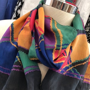 Peut inclure: Écharpe en soie colorée avec un motif géométrique dans les tons de bleu, orange, vert, violet et rouge. L'écharpe a une bordure noire et est drapée sur un mannequin. Accessoire de mode.