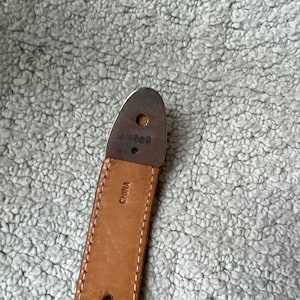 May include: Close-up of a brown leather belt with white stitching. The belt has a metal end piece with the number "1996" stamped on it. The word "CHINA" is also visible on the belt.