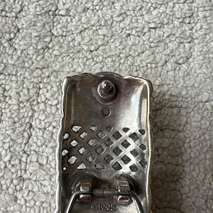 May include: Silver rectangular belt buckle with a decorative lattice pattern and a central stud. The buckle is attached to a brown leather belt. The year "1995" is stamped on the buckle.