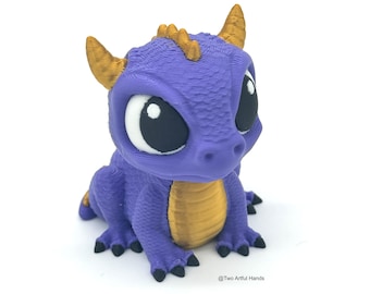 May include: A small, purple dragon figurine with gold accents and large, black eyes. The dragon is sitting on its hind legs with its front paws tucked in.