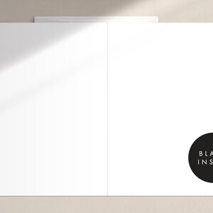 May include: A white greeting card with a blank interior, perfect for personalized messages. The card is displayed open, revealing the inside. A black circle with the words "BLANK INSIDE" is on the right side. The card is on a neutral background.