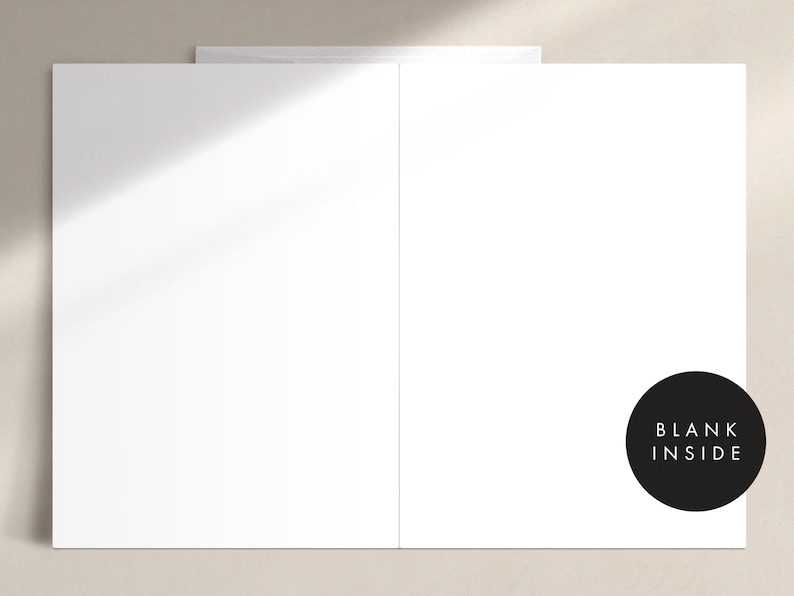 May include: A white greeting card with a blank interior, perfect for personalized messages. The card is displayed open, revealing the inside. A black circle with the words "BLANK INSIDE" is on the right side. The card is on a neutral background.