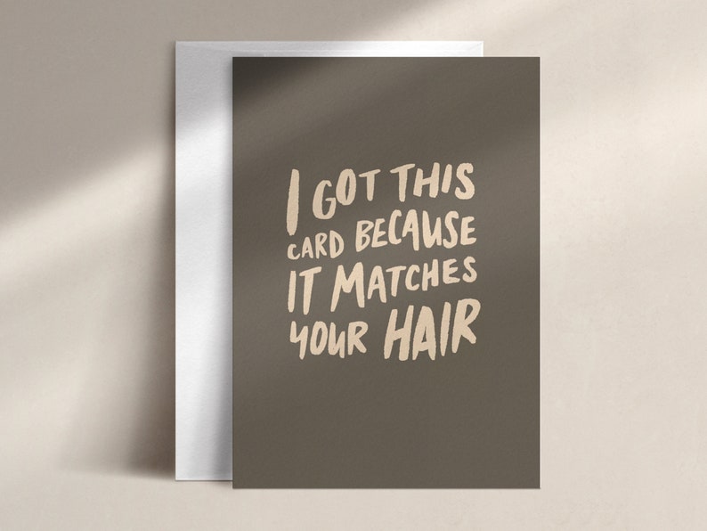 Może przedstawiać: Kartka okolicznościowa z napisem "I GOT THIS CARD BECAUSE IT MATCHES YOUR HAIR" w stylu ręcznym. Karta ma ciemno oliwkową zieleń i jest połączona z białą kopertą.