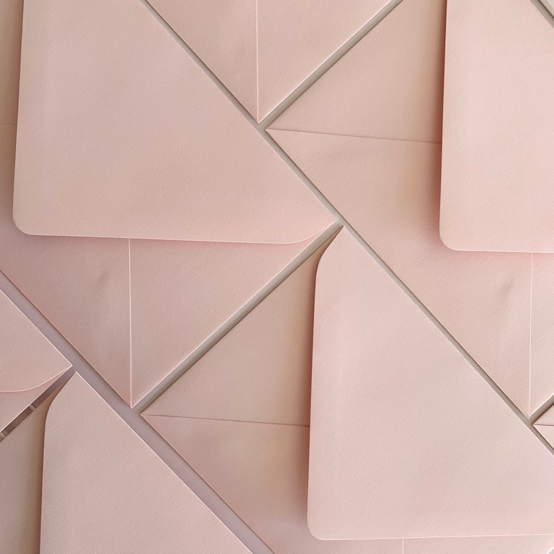 Puede incluir: Una pila de sobres de color rosa p&aacute;lido dispuestos en un patr&oacute;n geom&eacute;trico. Los sobres est&aacute;n doblados y superpuestos, creando un dise&ntilde;o visualmente interesante.