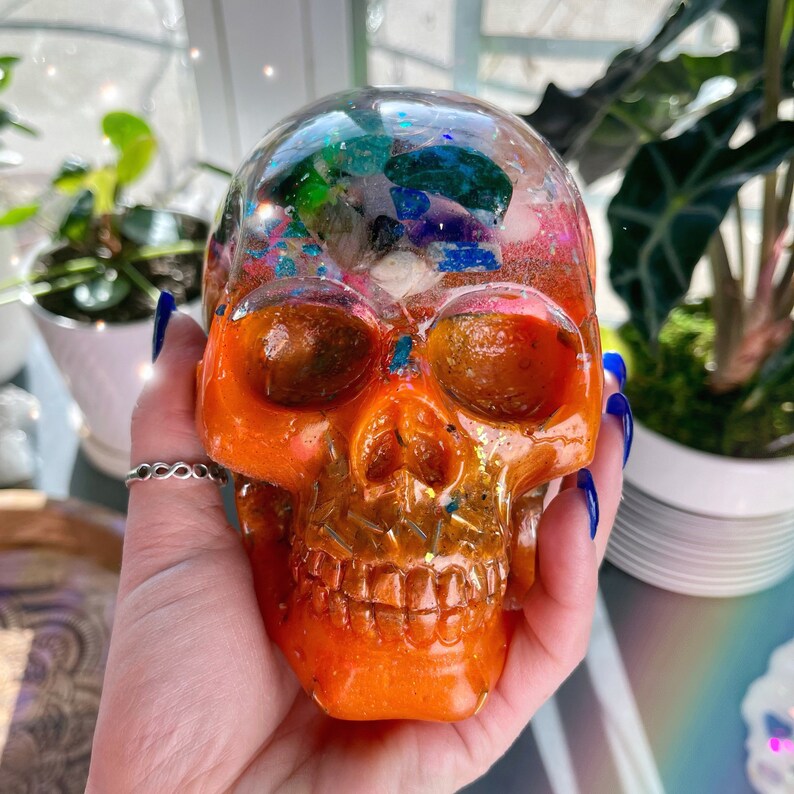 May include: Orange resin skull with a clear top filled with colorful glitter and crystals.