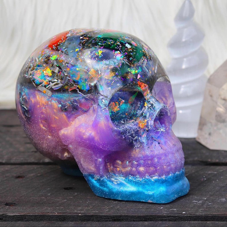 May include: A purple and blue resin skull with iridescent glitter and gold flakes embedded inside. The skull is a decorative object.