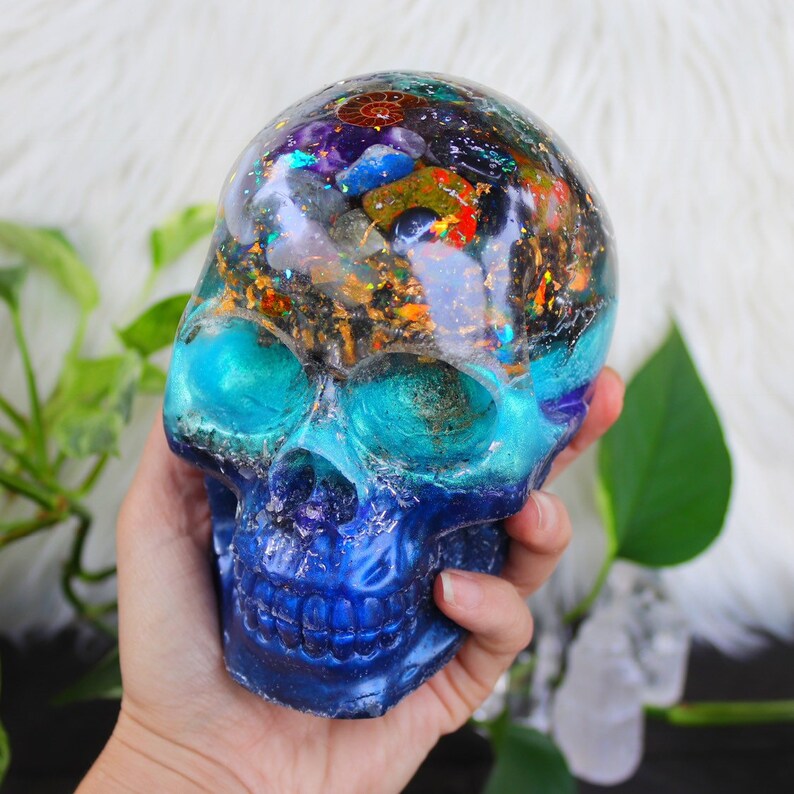 May include: A blue and green resin skull with a clear top filled with various crystals and stones. The skull is a decorative object.