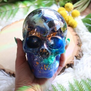 May include: A blue and green resin skull filled with various crystals and gold flakes. The skull is clear on top, showing the crystals inside.