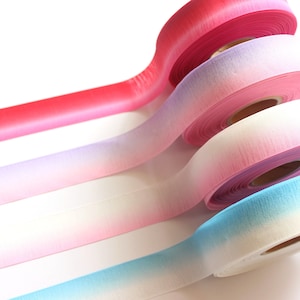 May include: Four rolls of ombre ribbon in pink, purple, white, and blue. The ribbon is made of a soft, textured material and is perfect for adding a touch of color and elegance to any project.