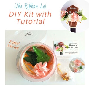 May include: A DIY kit for making a ukulele ribbon lei. The kit includes pink ribbon, green leaves, pink flowers, and yellow beads. The kit comes in a clear plastic container with a lid. The kit also includes a card with the company's logo and website information.
