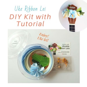 May include: A DIY kit for making a ukulele ribbon lei, with a clear container of blue, white, and yellow ribbon, green leaves, and a blue ribbon bow. The kit also includes a small bag of yellow beads and a card that says "Hawaiian crafts Ukulele Ribbon Leis".