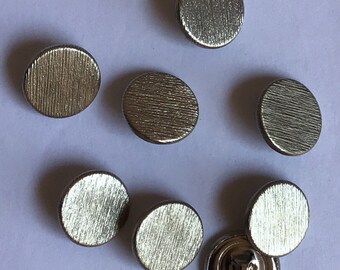 May include: Eight silver-toned buttons with a textured finish. The buttons are round and have a flat back.