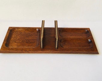 May include: A wooden valet tray with two gold-colored metal dividers and three compartments. The tray is made of dark wood and has a smooth finish.