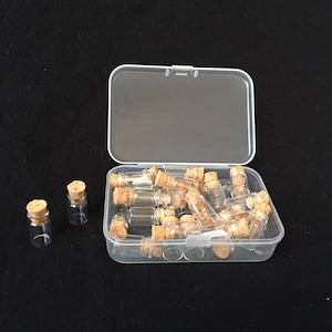 May include: A clear plastic box filled with small glass bottles with cork stoppers. The bottles are arranged in a random pattern. The box is sitting on a black surface.