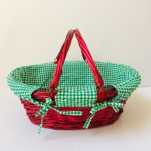 May include: A red wicker basket with green and white checkered fabric lining. The basket has two handles and is oval shaped.