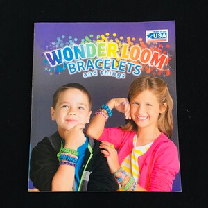 May include: A book cover with a rainbow design featuring the text "Wonder Loom Bracelets and things" and a star with the text "Made in the USA". Two children are smiling and wearing colorful bracelets.
