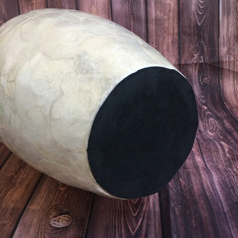 May include: A large, pear-shaped decorative vase with a cream-colored, textured exterior. The base of the vase is a solid black. The vase is set against a wooden background.