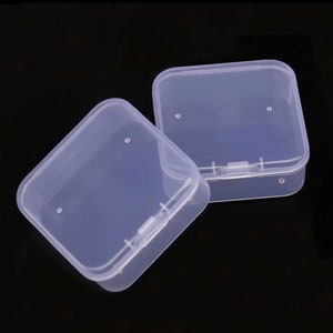 May include: Two clear plastic square storage boxes with hinged lids. The boxes have small holes on the top and a latch on the front.
