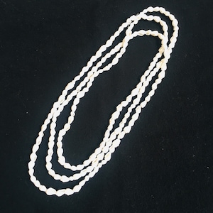 May include: A white shell necklace made of multiple strands of small, oval-shaped shells. The necklace is laid out on a black surface.