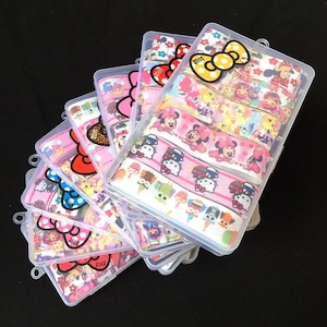 May include: A set of eight clear plastic boxes filled with colorful ribbon featuring cartoon characters like Hello Kitty and Mickey Mouse. The ribbon is pink, yellow, and blue with white accents.