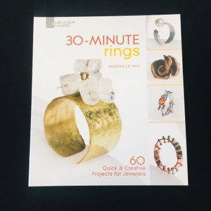 May include: Book cover for "30-Minute Rings" by Marthe Le Van. The cover features a gold ring with white stones and a variety of other rings. The book title is in large, bold letters and the subtitle is "60 Quick & Creative Projects for Jewelers".