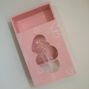 May include: Pink gift box with a heart-shaped window. The box has a white background with a pattern of hearts and the text "To Someone Special".