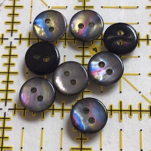 May include: Assortment of eight two-hole buttons in black and iridescent colors. The buttons have a smooth, shiny finish.