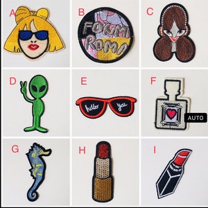 May include: Nine colorful embroidered iron-on patches. The patches feature a variety of designs, including a woman with sunglasses, a pair of sunglasses with the words "hello" and "you" on the lenses, a bottle of perfume, an alien, a seahorse, and a lipstick.