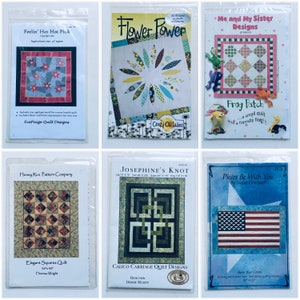 May include: Six quilt pattern designs in plastic packaging. The patterns include "Feelin' Hot Hot Pink", "Flower Power", "Frog Patch", "Elegant Squares Quilt", "Josephine's Knot", and "Pieces Be With You".