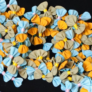 May include: A collection of handmade fabric bows in blue, yellow, and brown. The bows are arranged in a random pattern and are perfect for adding a touch of whimsy to any project.
