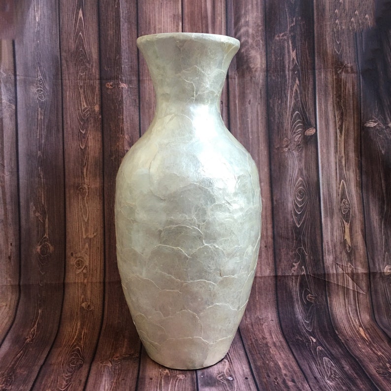 May include: A tall, pearlescent vase with a wide base and flared top. The vase has a textured surface with a subtle, organic pattern. The neutral color and elegant shape make it a versatile decorative piece.