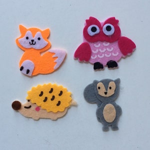 May include: Four felt animal appliques: a fox with an orange body and white face, an owl with pink feathers and black eyes, a hedgehog with a yellow body and brown spines, and a squirrel with a gray body and brown ears.