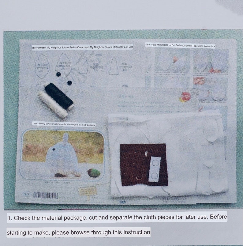 May include: A white fabric kit for making a Totoro plushie. The kit includes fabric pieces, thread, buttons, and instructions. The instructions include a diagram of the Totoro's body parts and a list of materials. The text on the instructions reads "Mengwuchi My Neighbor Totoro Series Ornament My Neighbor Totoro Material Pack List" and "Kitty Totoro Material Kit for Cat Series Ornament Production Instructions".