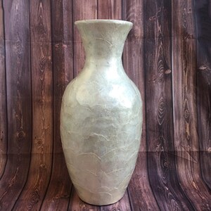 May include: A tall, pearlescent vase with a wide base and flared top. The vase has a textured surface with a subtle, crackled pattern. The neutral color and elegant shape make it a versatile decorative piece.