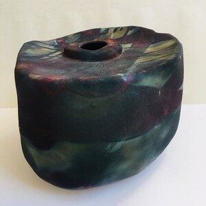 May include: A dark green and purple ceramic vase with an irregular shape and a round opening at the top.