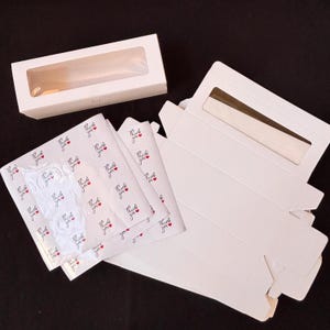 May include: White bakery boxes with clear window panels, alongside folded boxes and tissue paper printed with "Thank you" and small red hearts. Ideal for packaging baked goods.