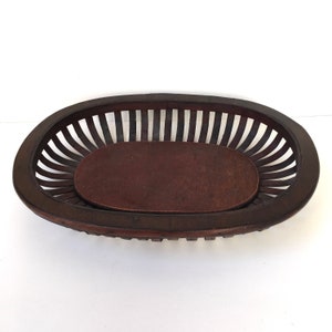 May include: A dark brown wooden oval basket with a slatted design and a solid wood bottom.