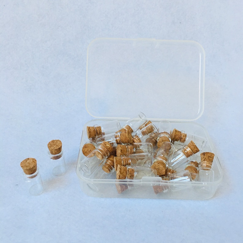 Puede incluir: Una caja de pl&aacute;stico transparente llena de peque&ntilde;as botellas de vidrio con tapas de corcho. Las botellas est&aacute;n dispuestas en un patr&oacute;n aleatorio.