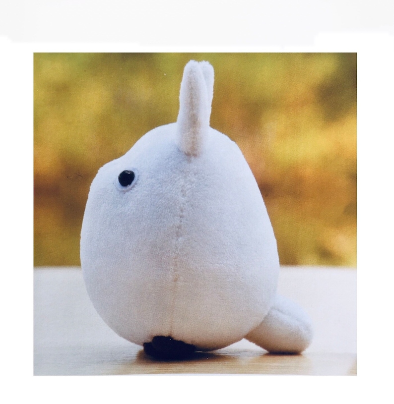 May include: A white plush toy shaped like a seal with a black eye. The toy is sitting on a wooden surface.