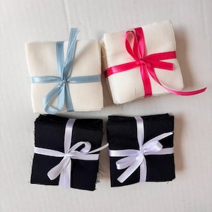 May include: Four stacks of fabric squares, each tied with a ribbon. The stacks are white with blue ribbon, white with pink ribbon, black with white ribbon, and black with white ribbon.