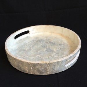 May include: A round, white tray with two handles made of mother of pearl. The tray has a textured surface and is perfect for serving snacks or drinks.