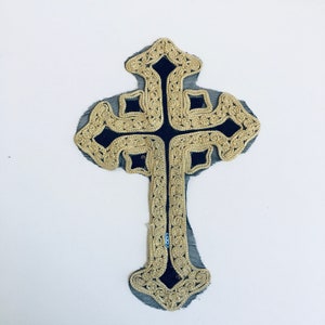 May include: A gold and black cross with intricate detailing. The cross is made of fabric and has a velvet-like texture.