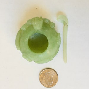 May include: A small, green jade bowl with a carved design and a matching jade spoon. The bowl is about the size of a US quarter.
