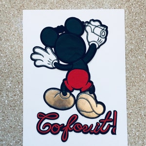 May include: A black and red cartoon character with large ears and white gloves. The character is holding a camera and is standing on a white background. The text "Go for it!" is written in red below the character.