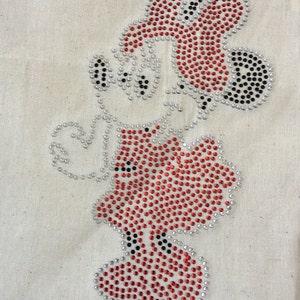 May include: A red and black rhinestone design of a cartoon character. The character is wearing a hat and has a large nose.