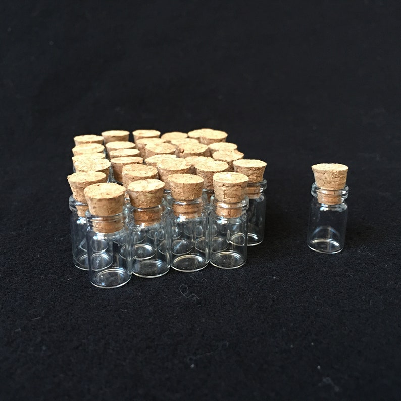 Puede incluir: Un grupo de peque&ntilde;as botellas de vidrio transparente con tapones de corcho. Las botellas est&aacute;n dispuestas en forma rectangular, con una botella sola a la derecha.