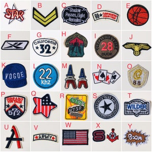 May include: A collection of 25 iron-on patches featuring various designs, including a star, a chevron, a basketball, a hat, a Eiffel Tower, a playing card, a bird, a star with the text "California 32", a star with the text "Star", a star with the text "Army", a star with the text "Wilder Than You Think", a star with the text "Space 1998 Authentic", a star with the text "Gibrano Vintage 572", a star with the text "22 khz", a star with the text "99* Campaviation Specialteam", a star with the text "Truegaizirtese 28 Duck", a star with the text "Shadow Passes, Light Remains", a star with the text "Vogue", a star with the text "Boom", a star with the text "CJD TSR", a star with the text "88", a star with the text "S", a star with the text "A", a star with the text "Reebok", a star with the text "A", a star with the text "S", a star with the text "A".